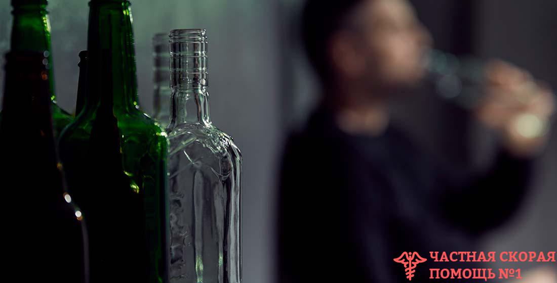 две бутылки алкоголя на фоне пьющего мужчины